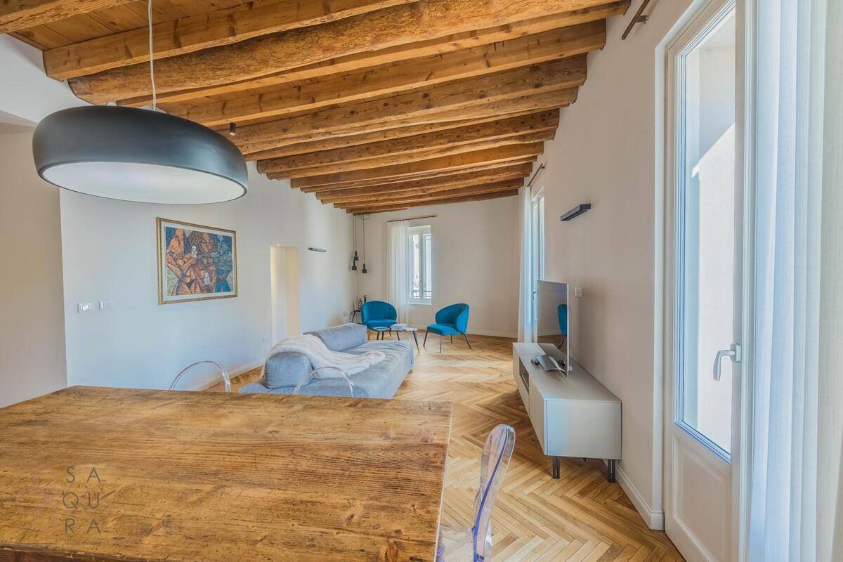 Wohn-Essbereich mit Holzbalkendecke, Fischgrätparkett und Zugang zu einem französischen Balkon.