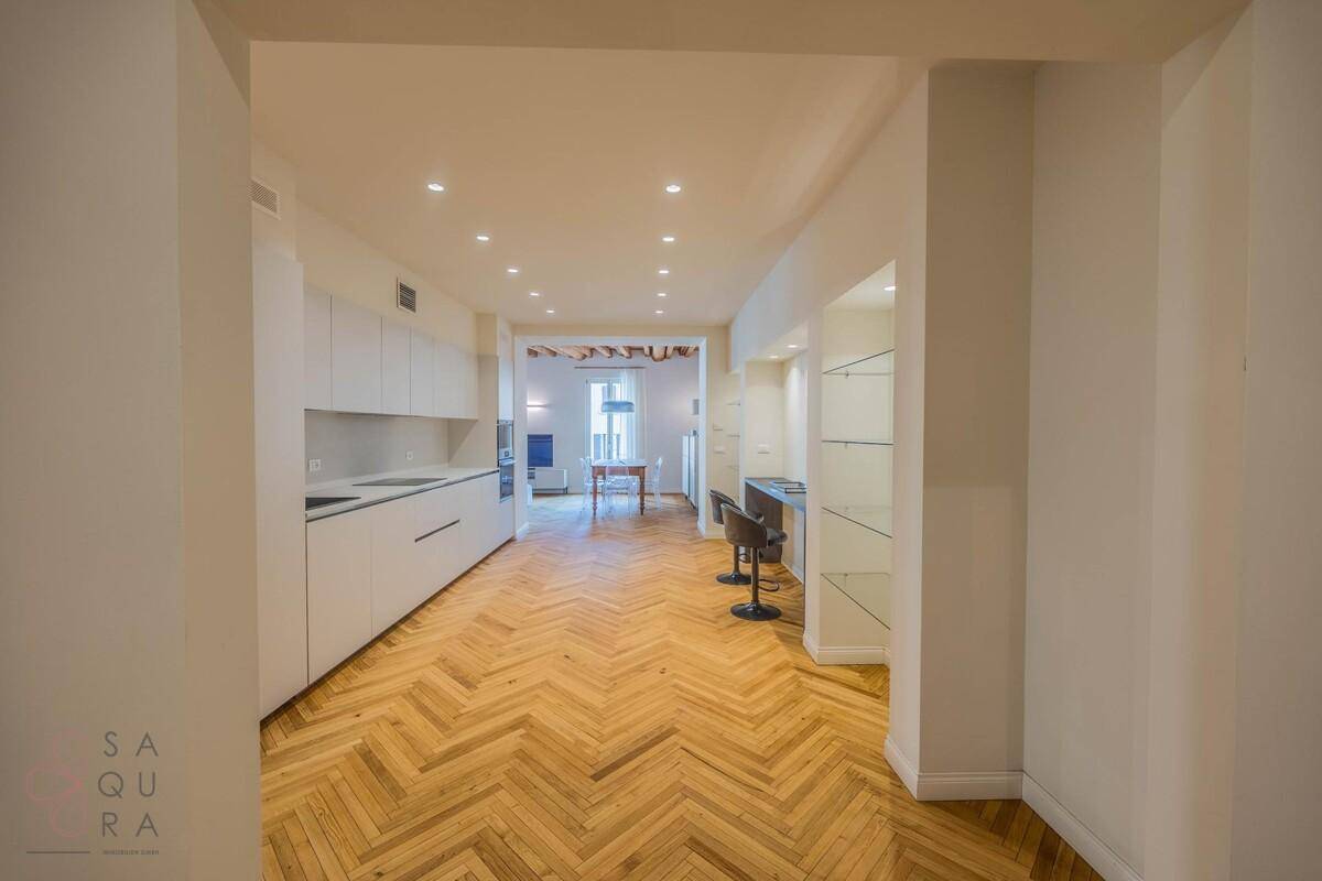 Moderne, offene Küche mit weißen Schränken, Fischgrätparkett und integriertem Essbereich.
