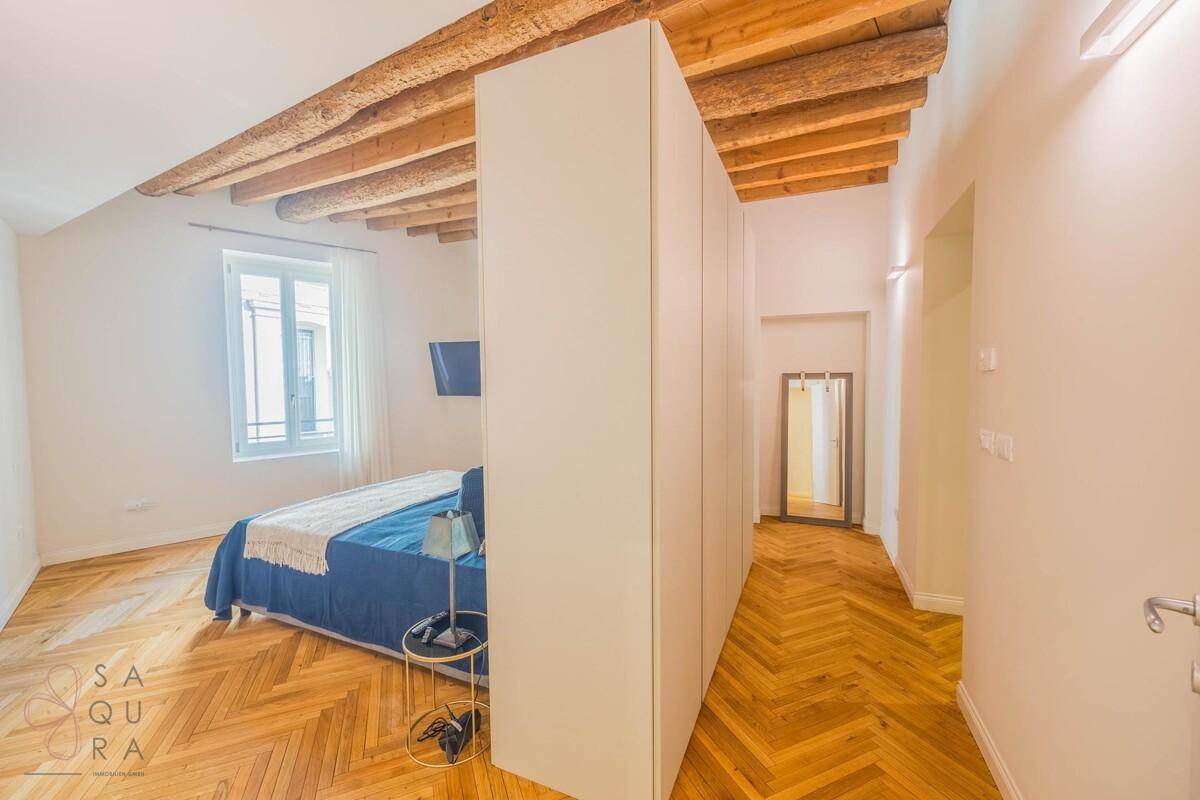 Schlafzimmer mit Holzbalkendecke, Fischgrätparkett und einem großen Kleiderschrank als Raumteiler.