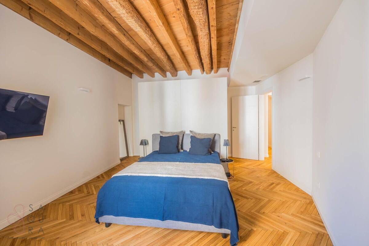 Helles Schlafzimmer mit Holzbalkendecke, Fischgrätparkett und einem Doppelbett.