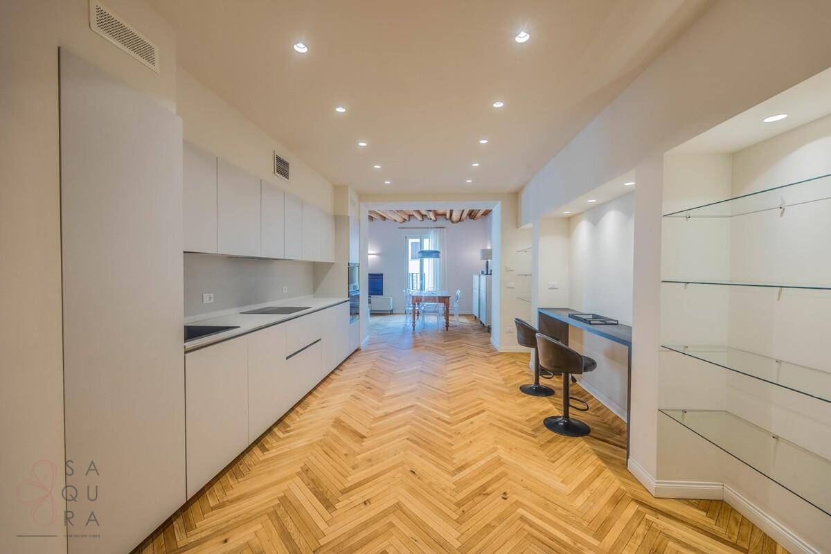 Moderne Küche mit weißen Schränken, Fischgrätparkett und einer Frühstücksbar mit Hockern.