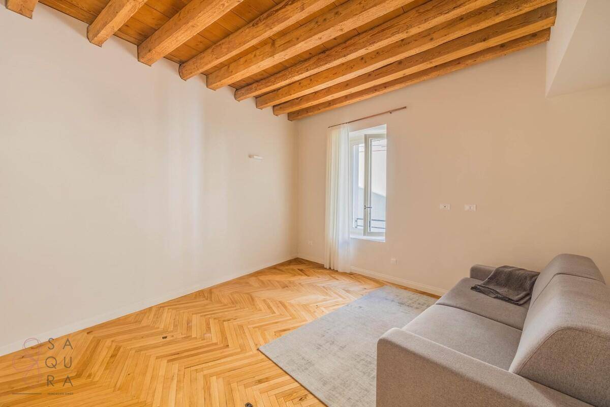 Helles Zimmer mit Holzbalkendecke, Fischgrätparkett und einem Schlafsofa.