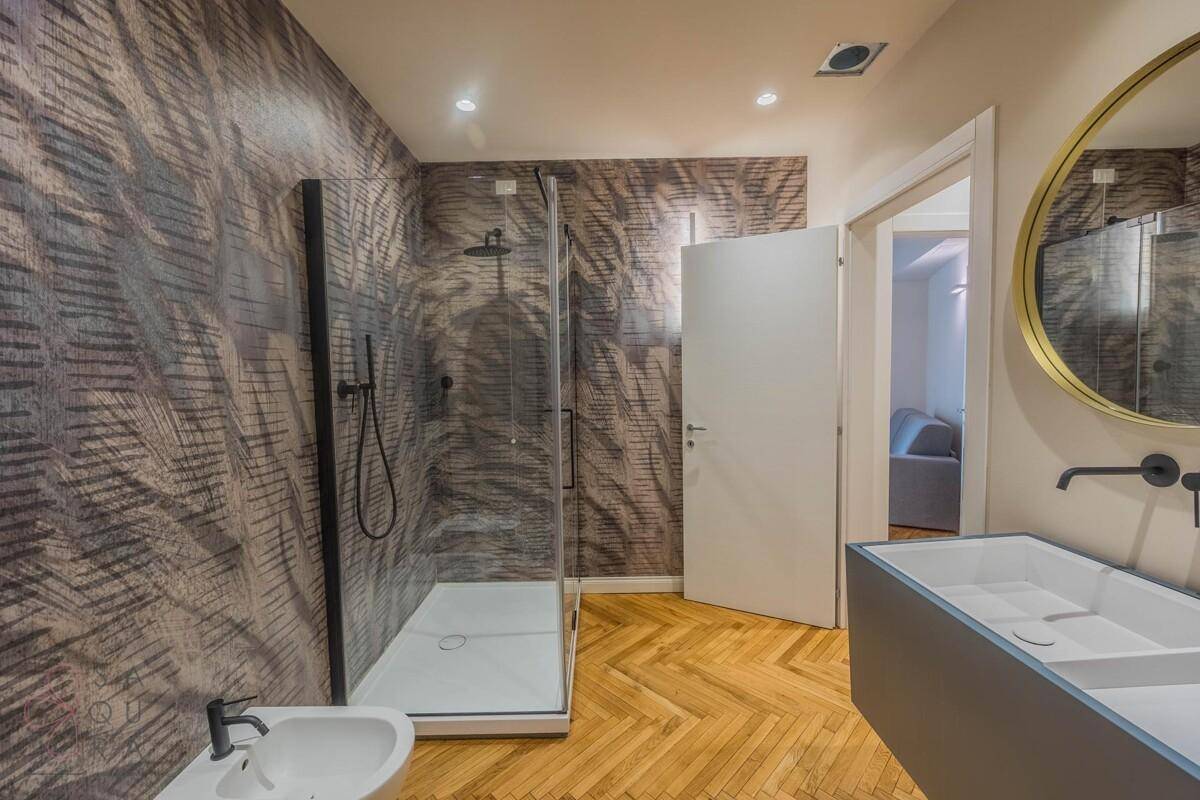 Modernes Badezimmer mit Duschkabine, Bidet, Aufsatzwaschbecken und rundem Spiegel.