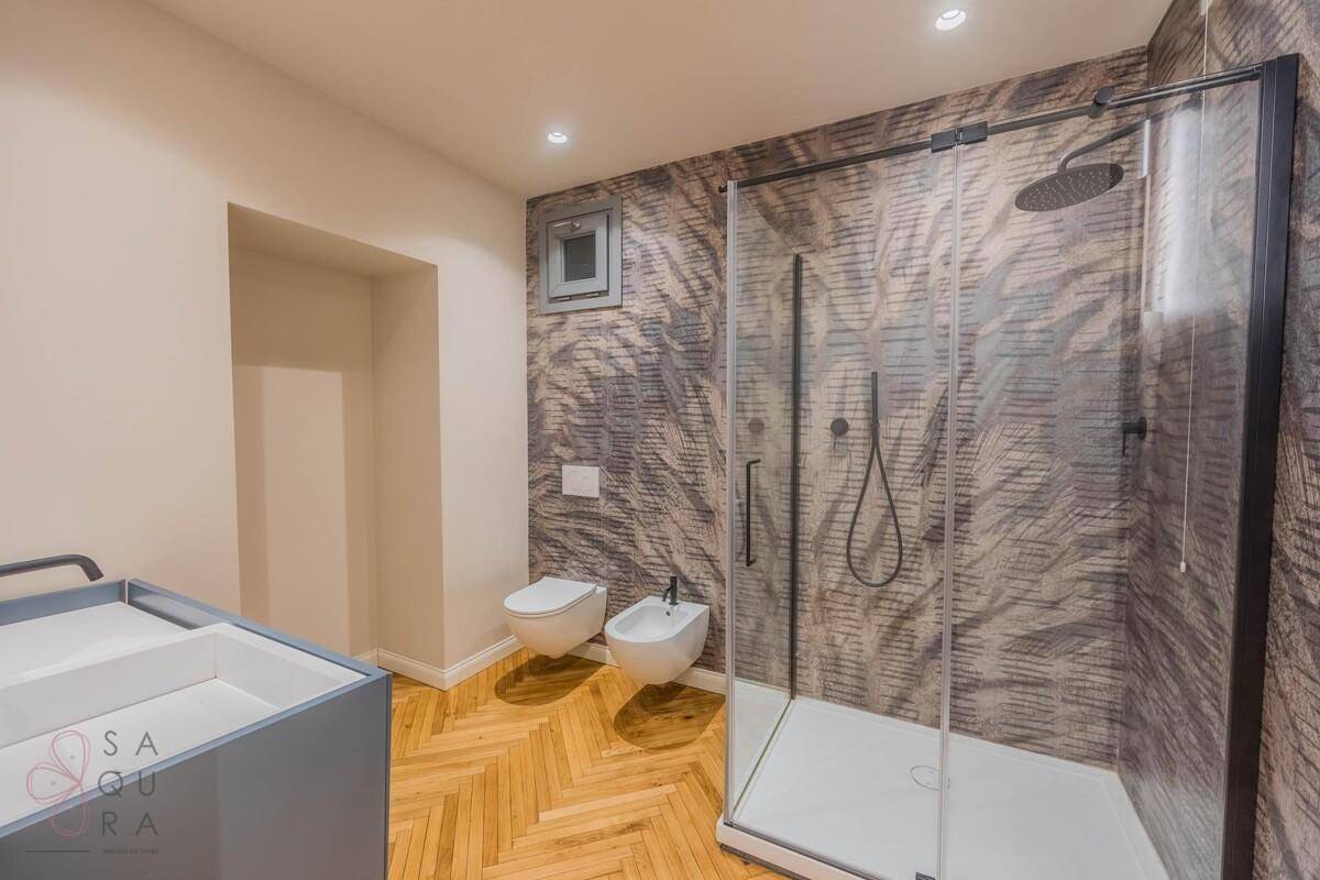 Modernes Badezimmer mit Duschkabine, Wand-WC, Bidet und gemusterten Wänden.