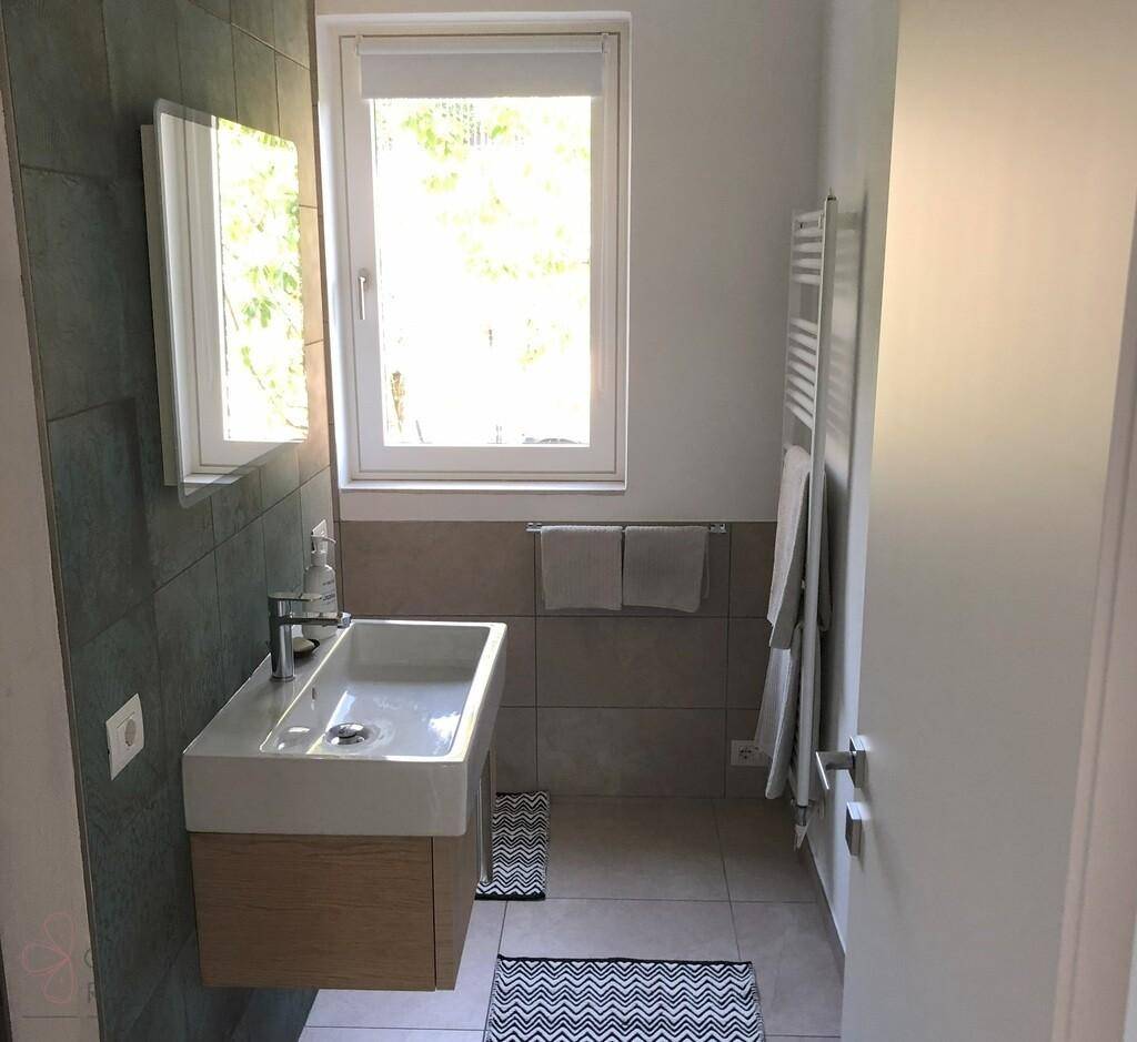 Modernes Badezimmer mit Wandwaschbecken, großformatigen Fliesen und Fenster.