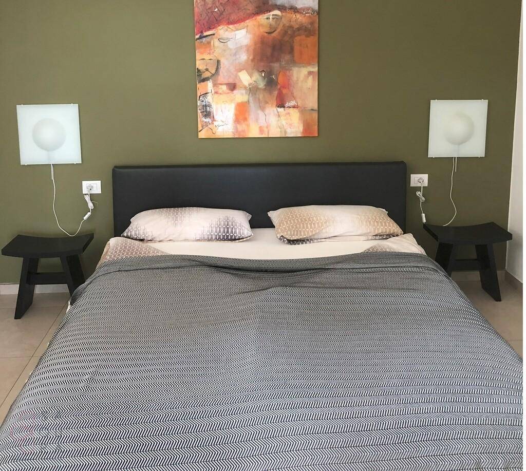 Schlafzimmer mit Doppelbett, grüner Akzentwand und moderner Kunst über dem Kopfteil.