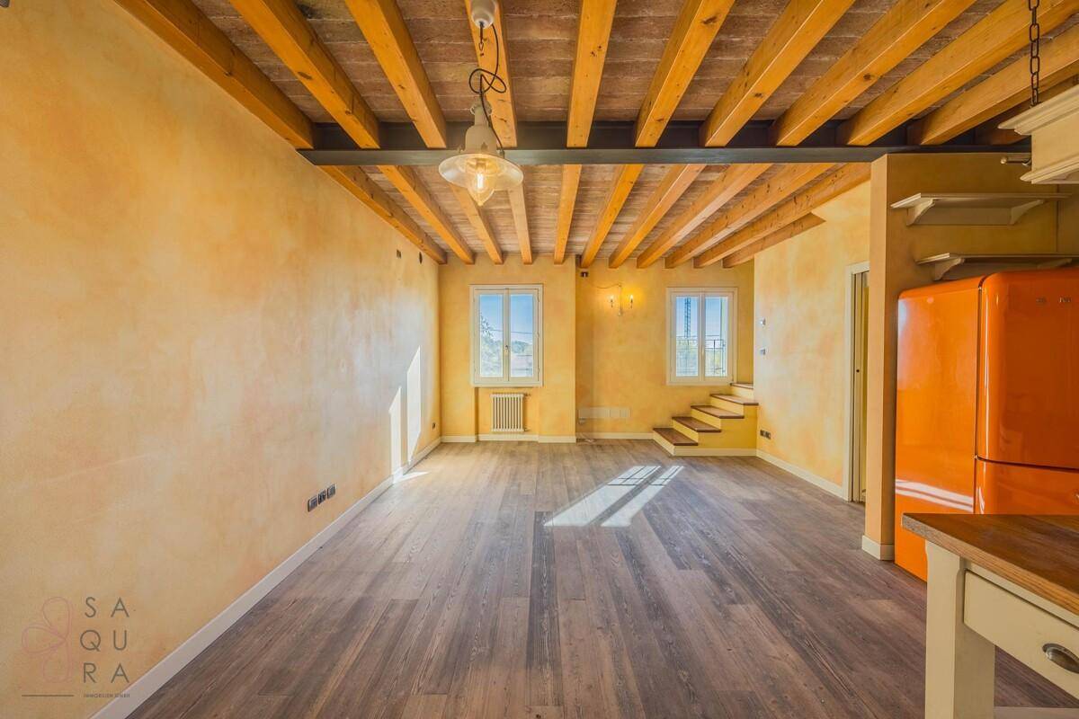 Heller Wohnbereich mit Holzboden, Holzbalkendecke und warmen gelben Wänden.