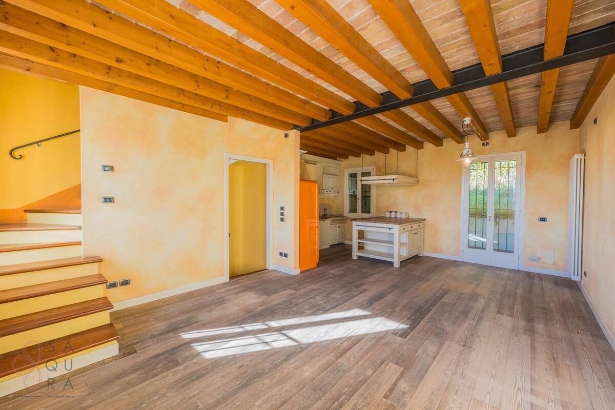 Offener Wohnbereich mit Holzboden, Holzbalken, Treppenaufgang und Zugang zum Außenbereich.