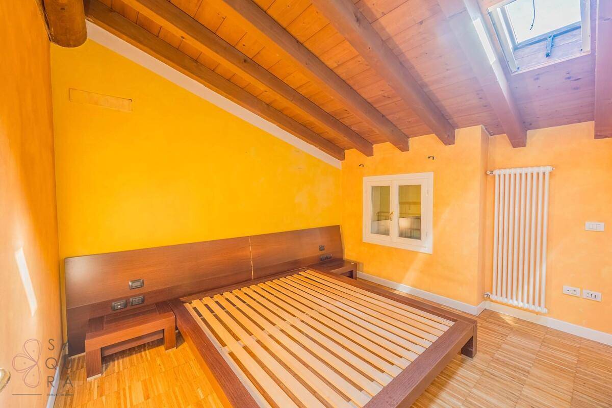 Schlafzimmer mit Holzbalkendecke, Dachfenster, gelben Wänden und Holzboden.