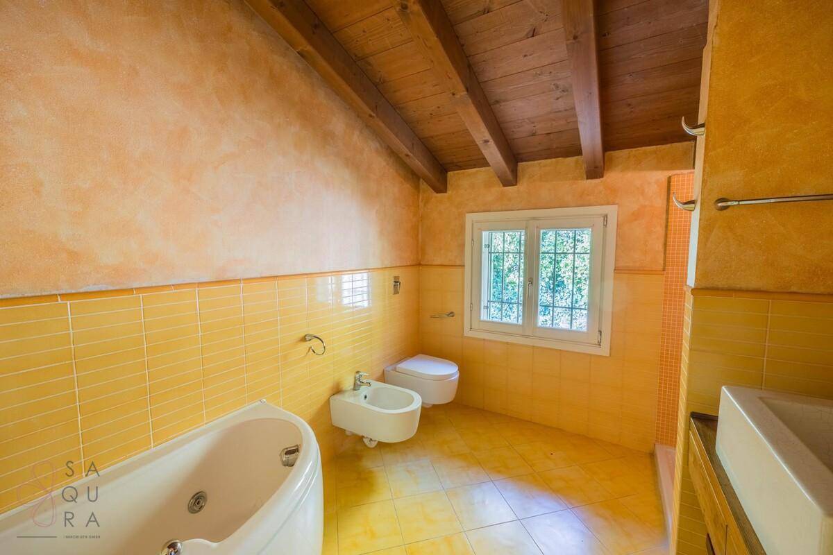 Geräumiges Badezimmer mit gelben Fliesen, Holzbalkendecke, Badewanne und Fenster.