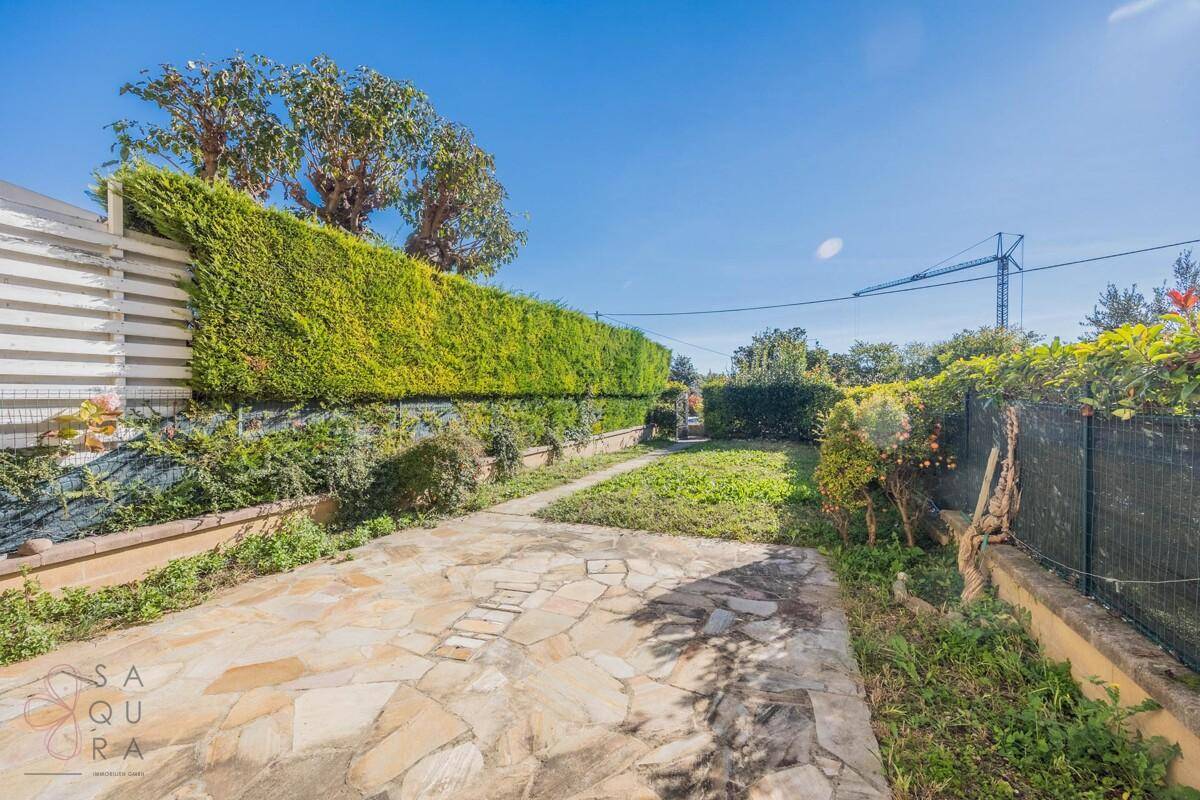 Gepflegter Gartenbereich mit Rasenfläche, Hecke und gepflastertem Sitzbereich.