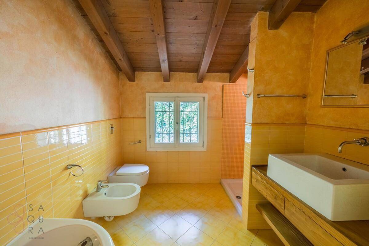 Helles Badezimmer mit gelben Fliesen, Holzbalkendecke, Badewanne, Bidet und Dusche.