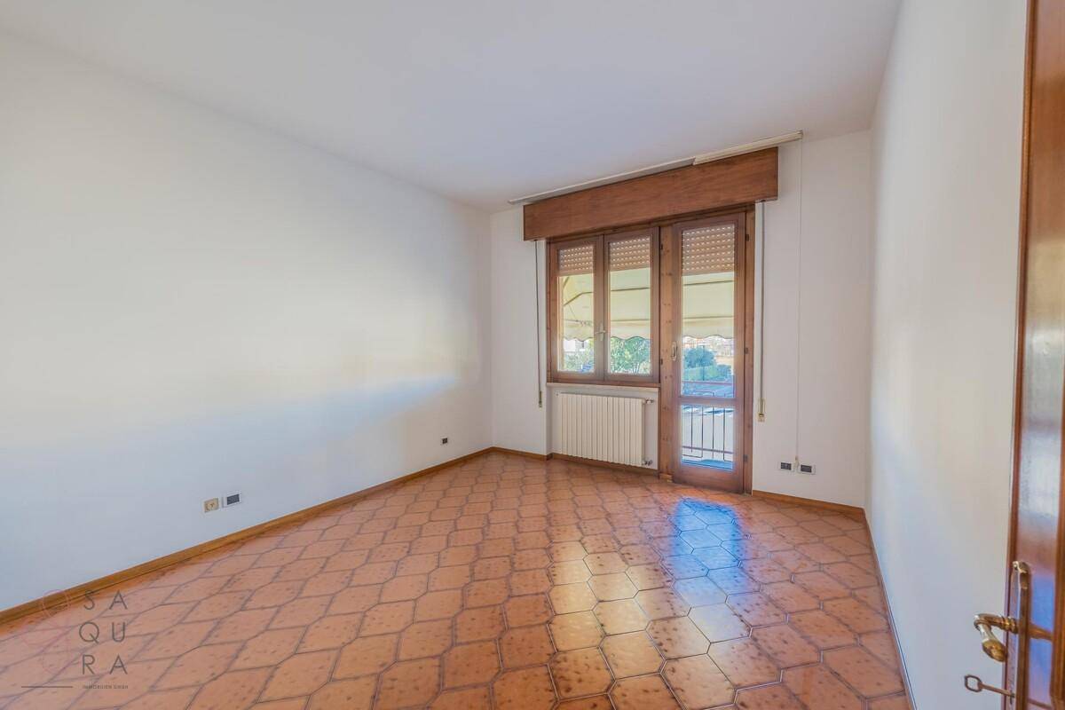 Leeres Schlafzimmer mit gemustertem Fliesenboden und Fenster mit französischem Balkon.