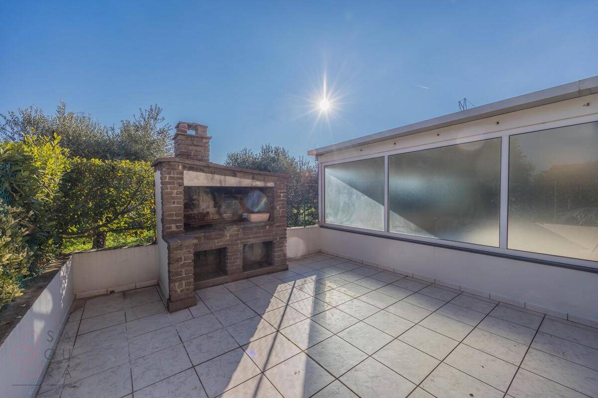 Helle Terrasse mit gemauertem Grill und Fliesenboden, ideal für Mahlzeiten im Freien unter der Sonne.