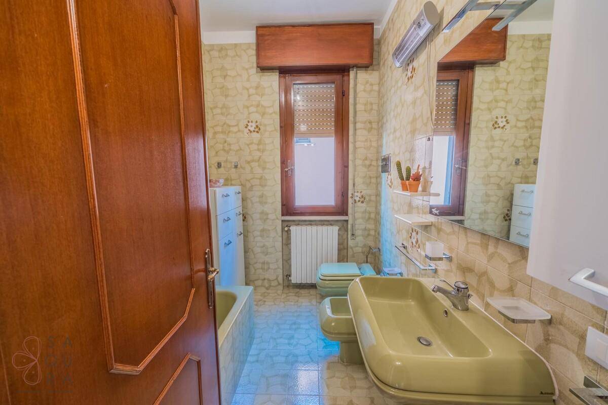 Badezimmer im 80er-Jahre-Stil mit Badewanne, WC und Waschbecken, dekoriert mit gemusterten Fliesen.