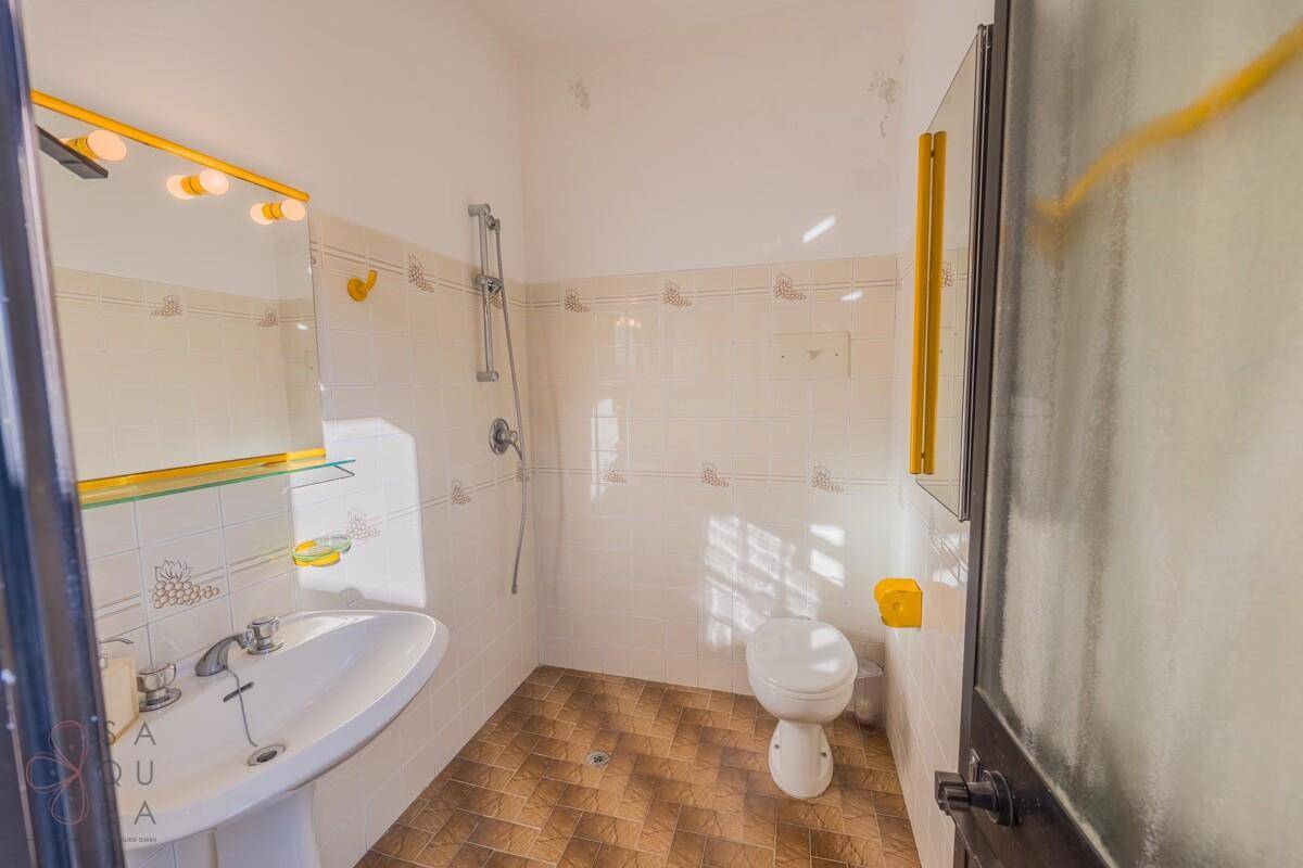 Helles Badezimmer mit Duschbereich, WC und Waschbecken, ausgestattet mit weißen Fliesen und gelben Akzenten.