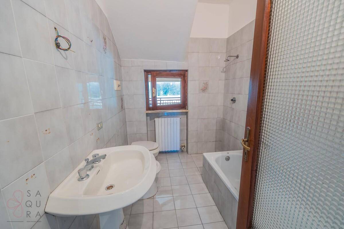 Badezimmer mit hellgrauen Fliesen, Waschbecken, Toilette, Bidet und Badewanne sowie einem Fenster.