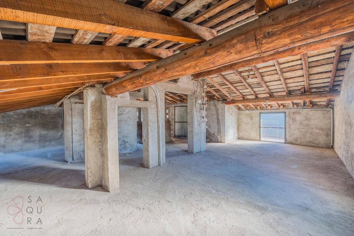 Unausgebauter Dachboden mit sichtbaren Holzbalken und Betonboden, bietet Ausbaupotenzial.