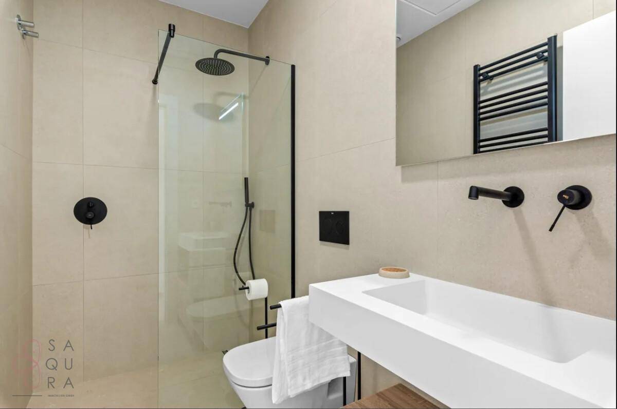 Modernes Badezimmer mit ebenerdiger Dusche, beheiztem Handtuchhalter und minimalistischen Armaturen.