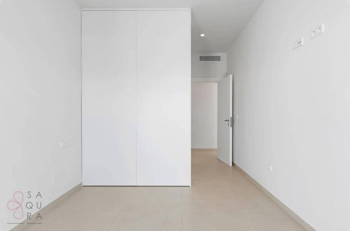 Schlichtes, helles Zimmer mit integriertem Kleiderschrank und Zugang zu einem weiteren Raum.