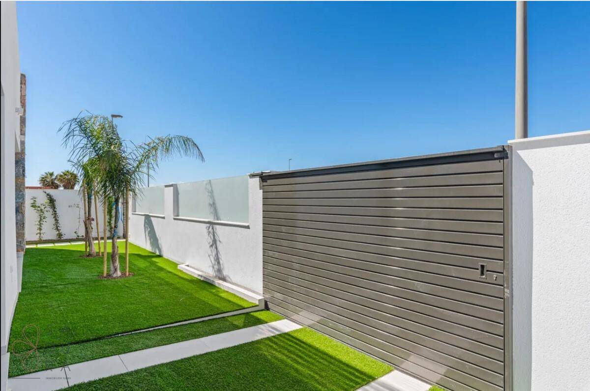 Seitlicher Gartenbereich mit Kunstrasen und einem modernen, grauen Schiebetor.