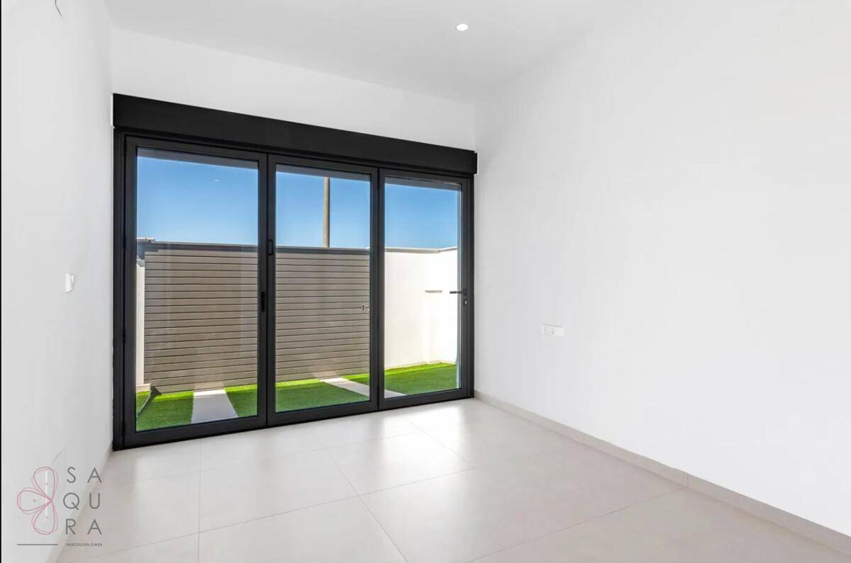 Leeres Zimmer mit großen Glasschiebetüren, die viel Tageslicht hereinlassen und einen Außenbereich zeigen.
