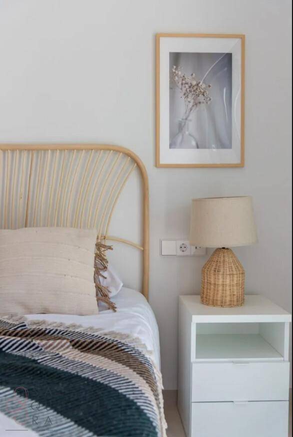 Helles Schlafzimmer mit Rattan-Kopfteil, Nachttisch und dekorativem Bild an der Wand.