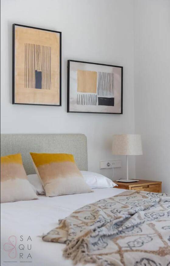 Modern eingerichtetes Schlafzimmer mit farbigen Kissen und abstrakten Bildern über dem Bett.