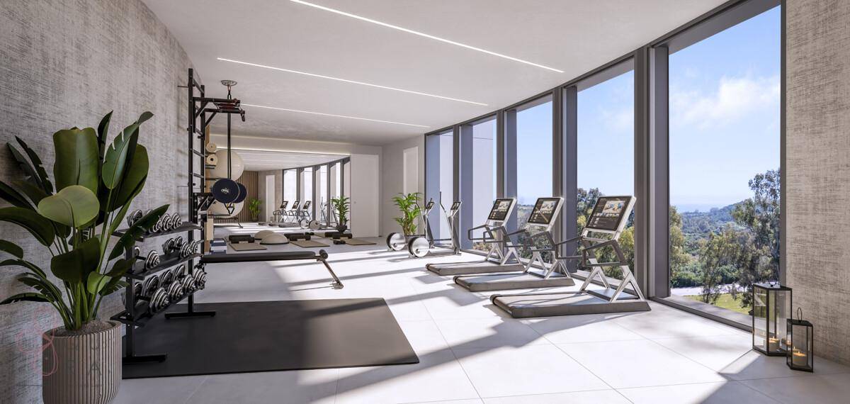 Moderner Fitnessraum mit verschiedenen Trainingsgeräten und großen Fenstern mit Blick ins Grüne.