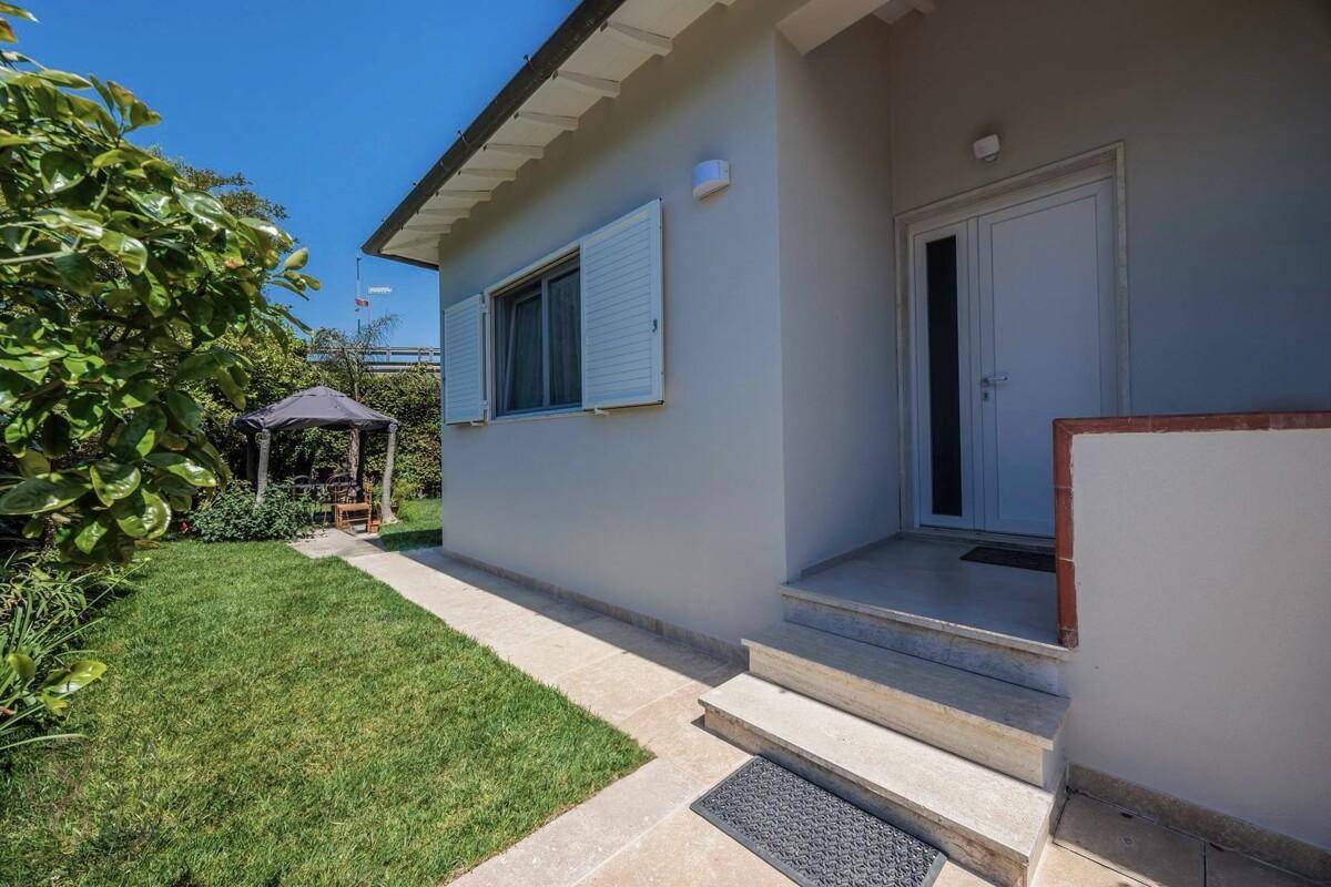 Eingangsbereich des Hauses mit Stufen, gepflegtem Rasen und einem Pavillon im Hintergrund.