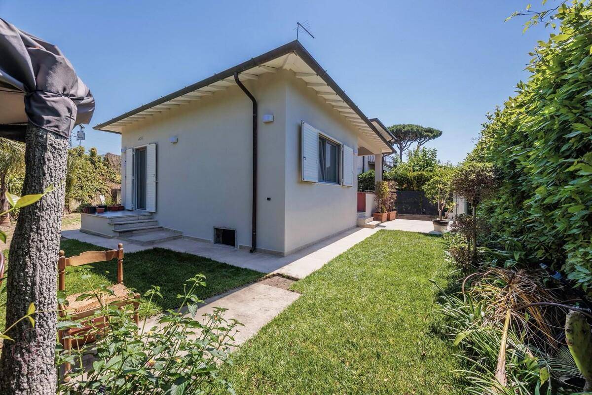 Rückseite des Hauses mit Rasenfläche, Bäumen und einem Stuhl im Vordergrund.