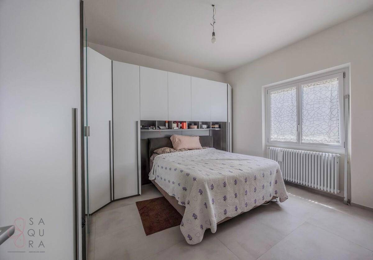 Schlafzimmer mit großem Fenster, Heizkörper und weißen Einbauschränken.