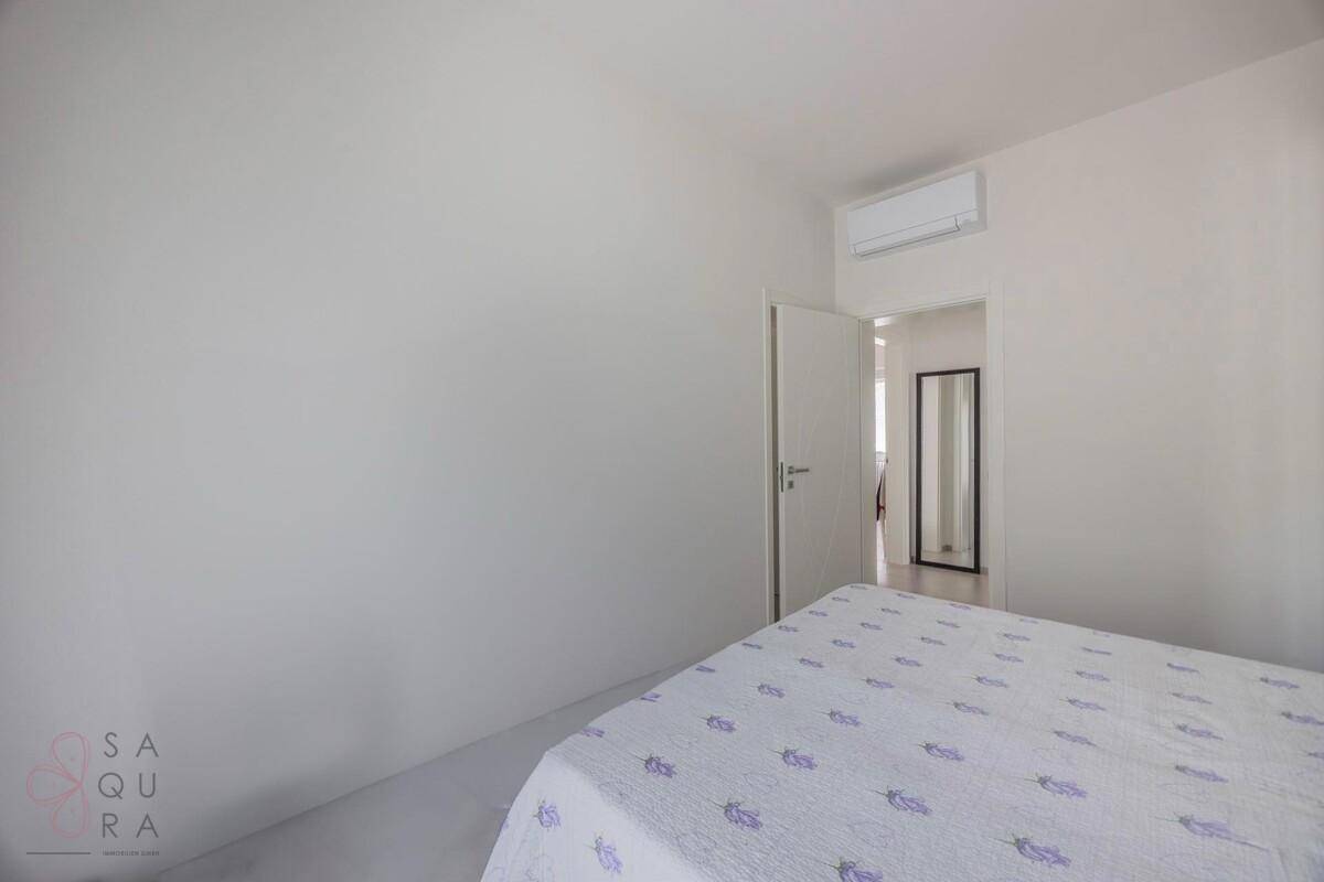 Schlafzimmer mit weiß gestrichenen Wänden, Klimaanlage und Blick in einen angrenzenden Raum.