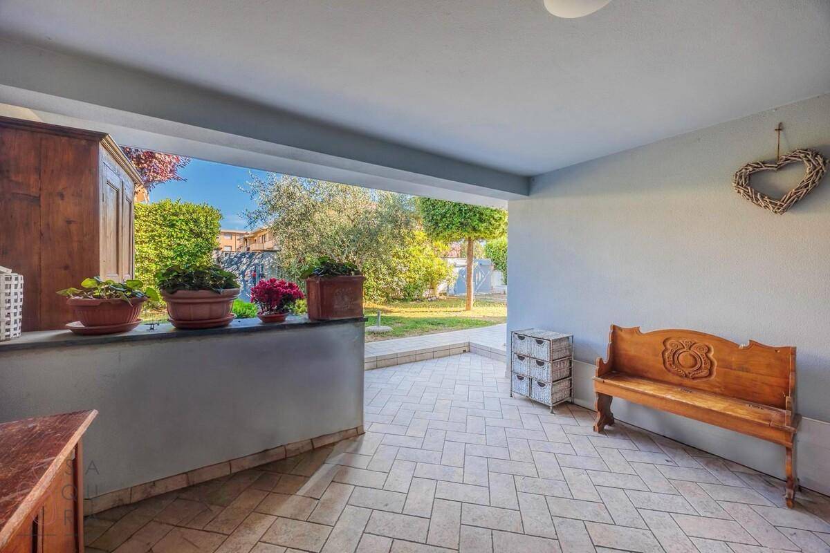 Überdachte Terrasse mit Fliesenboden, Holzbänken und Blick auf den grünen Garten.
