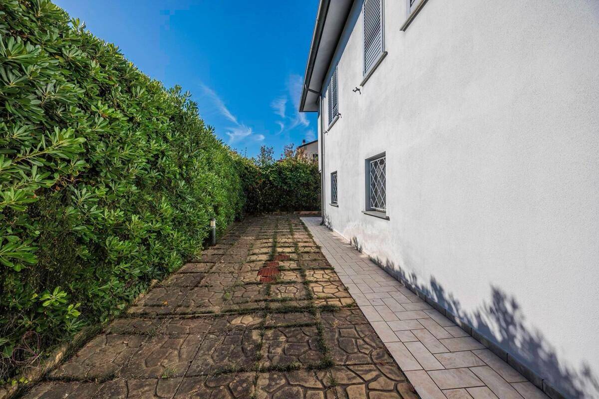 Langer gepflasterter Weg entlang einer hohen grünen Hecke, der zum Haus führt.