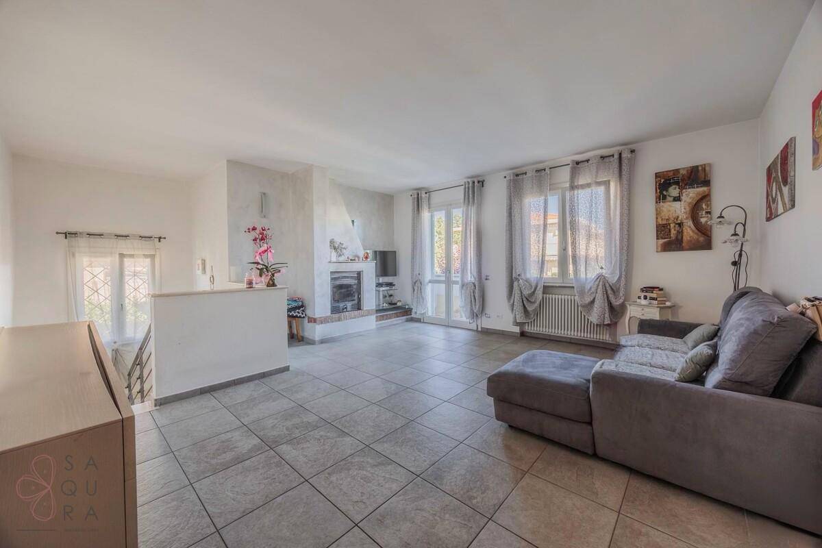 Geräumiges Wohnzimmer mit Fliesenboden, Kamin und bequemer grauer Eckcouch.