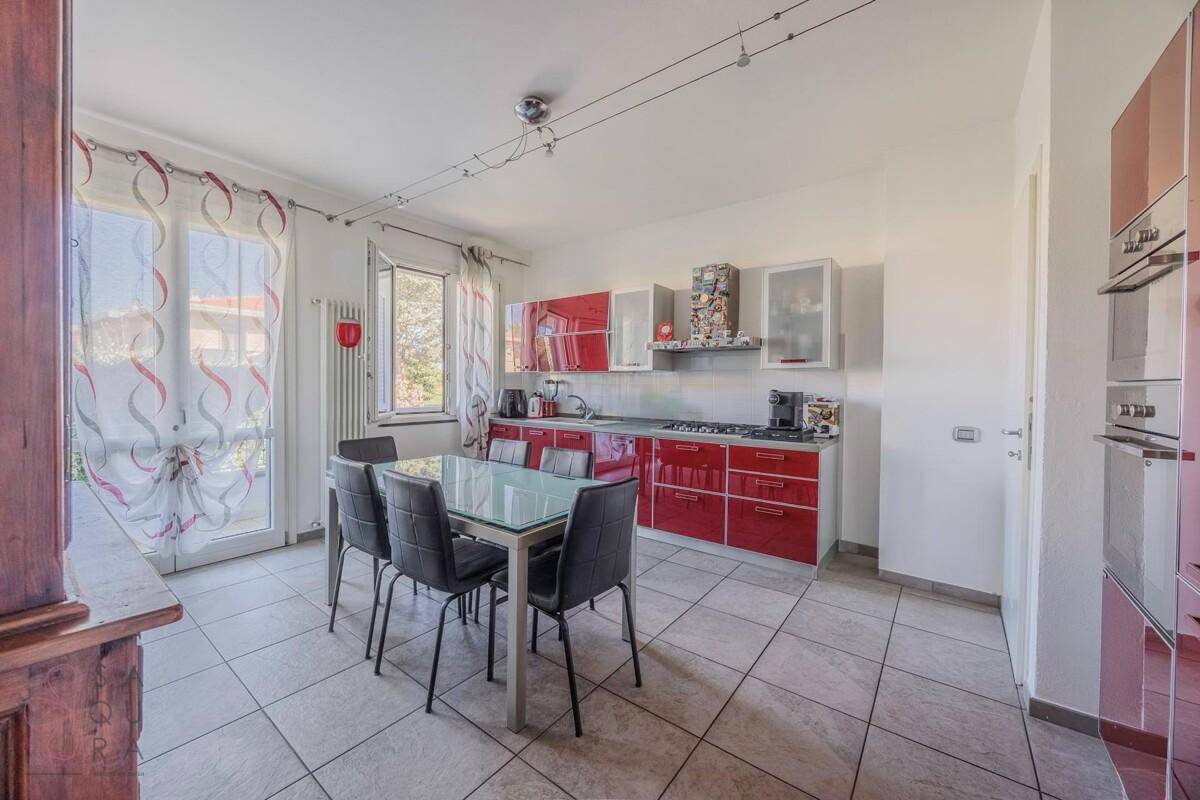 Moderne Küche mit roten Hochglanzfronten, Esstisch und Zugang zum Balkon.