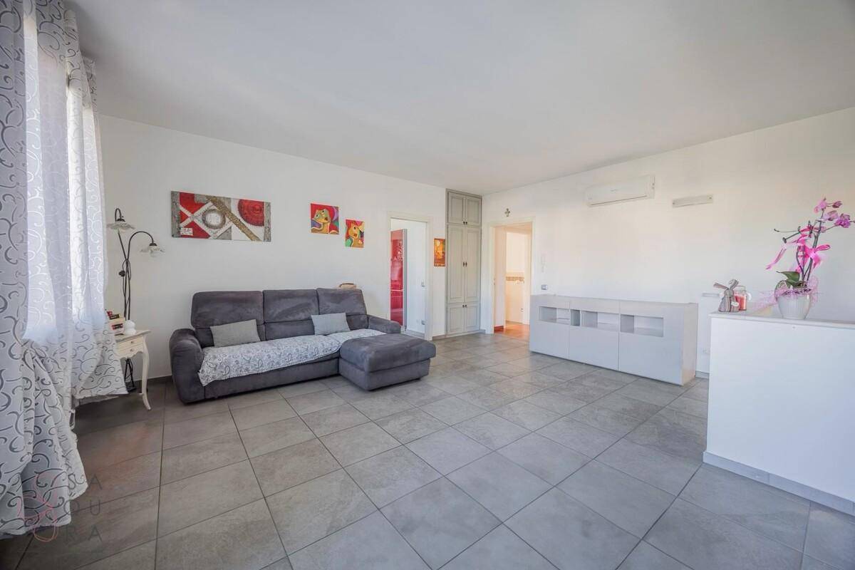 Helles Wohnzimmer mit Fliesenboden, Klimaanlage und moderner grauer Couch.