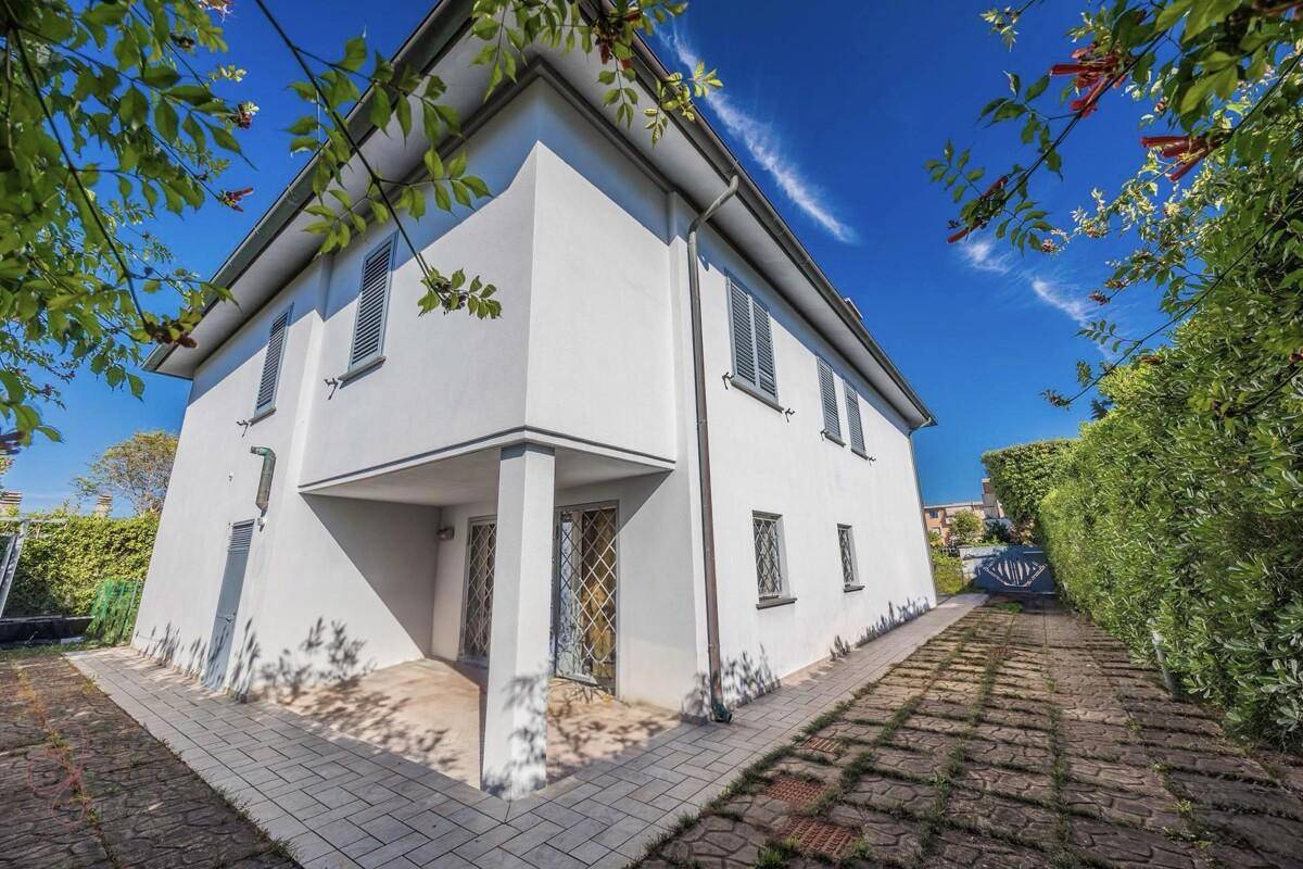 Seitenansicht des weißen Hauses mit gepflastertem Weg und grüner Hecke unter strahlend blauem Himmel.