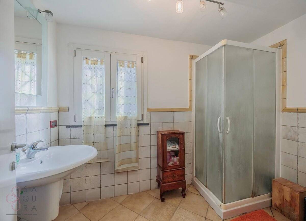 Badezimmer mit Duschkabine, Waschbecken und Fenster, gefliest in hellem Design.