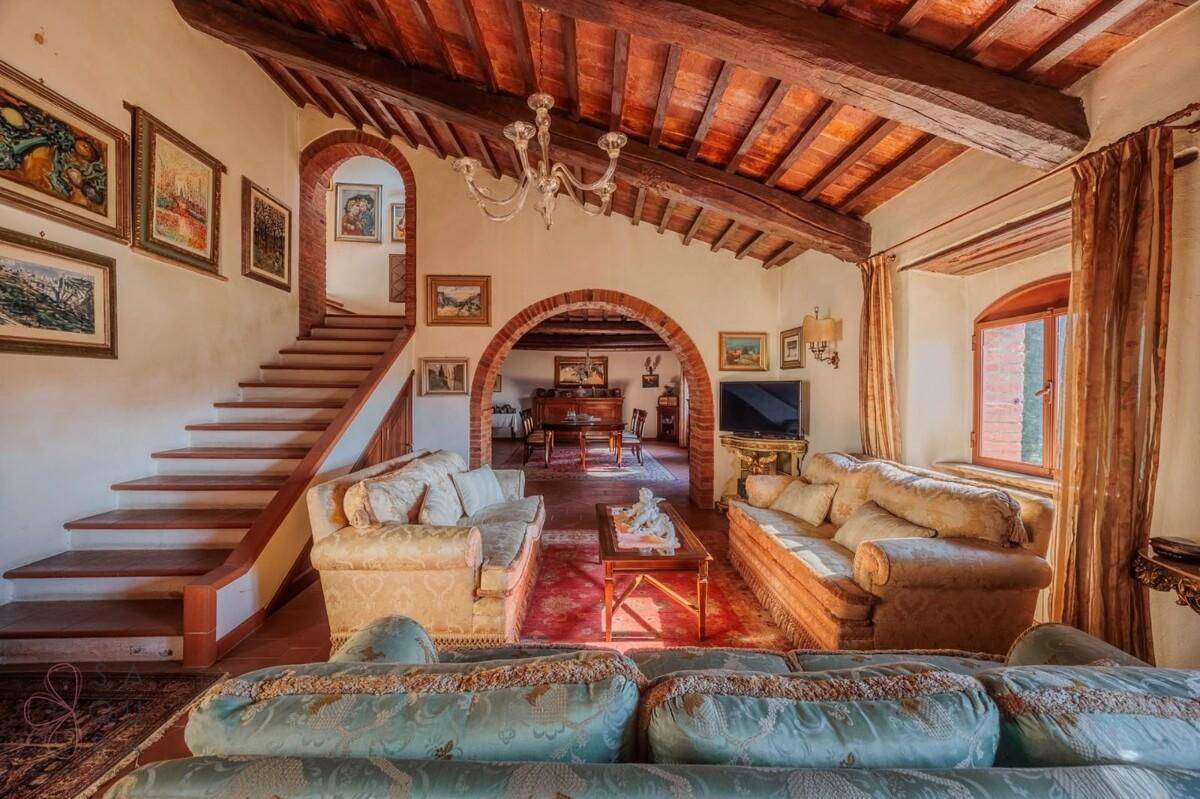 Gemütliches Wohnzimmer mit Holzbalkendecke, traditionellen Möbeln und Zugang zu einer Treppe.