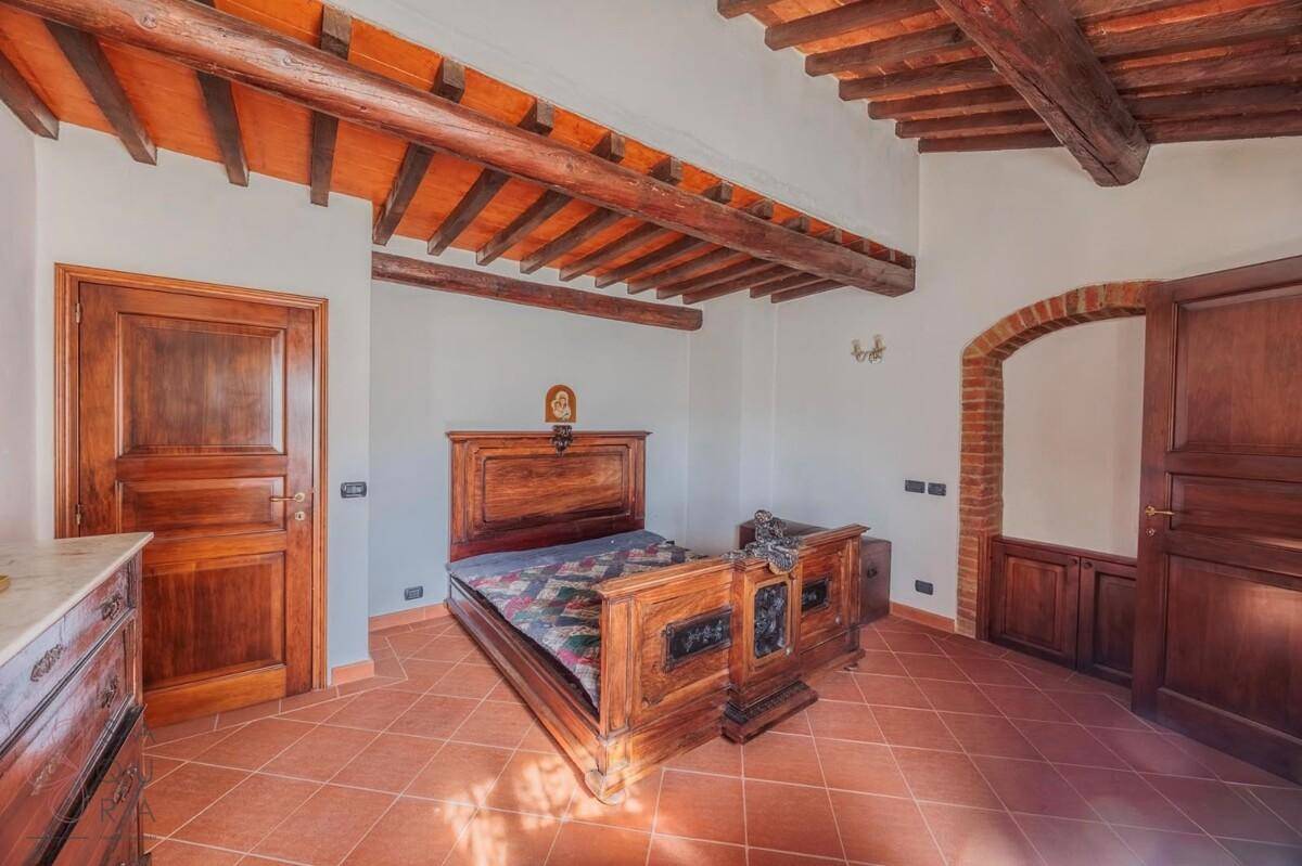 Schlafzimmer mit antikem Holzdoppelbett, Holzbalkendecke und Terrakottafliesen, strahlt rustikalen Charme aus.