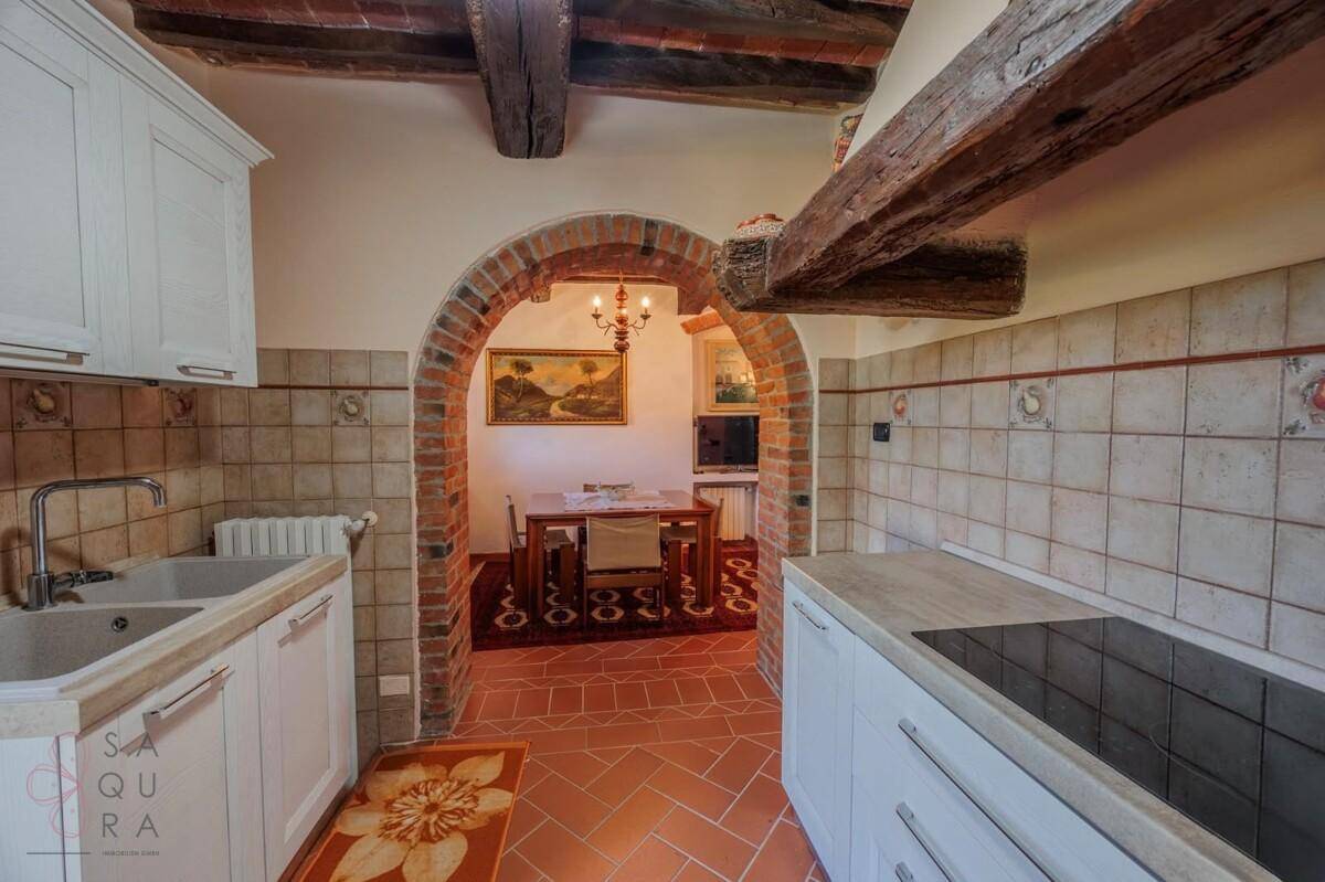 Funktionale Küche mit weißen Schränken, Terrakottafliesen und Blick in einen angrenzenden Essbereich.