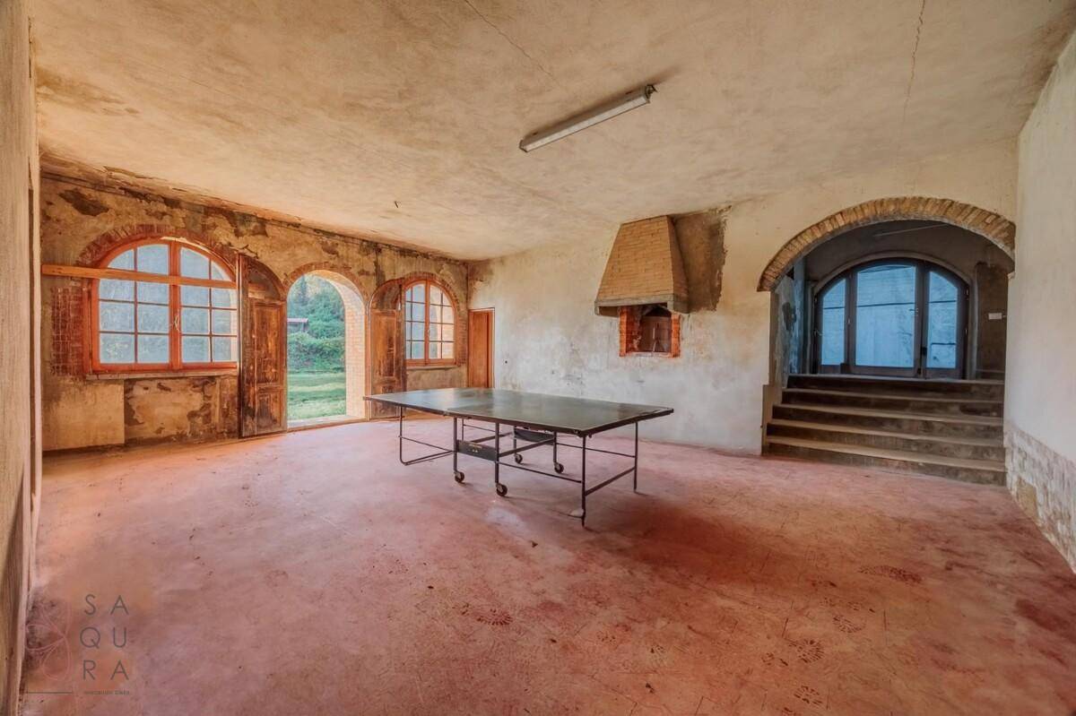 Großer, rustikaler Raum mit Bogenfenstern, Kamin und Tischtennisplatte, renovierungsbedürftig.