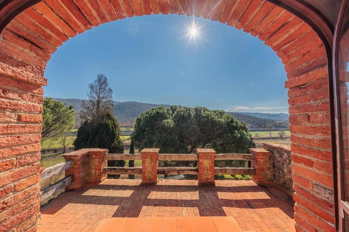 Sonniger Terrassenbereich mit Ziegelbogen und weitem Blick über die grüne Hügellandschaft.