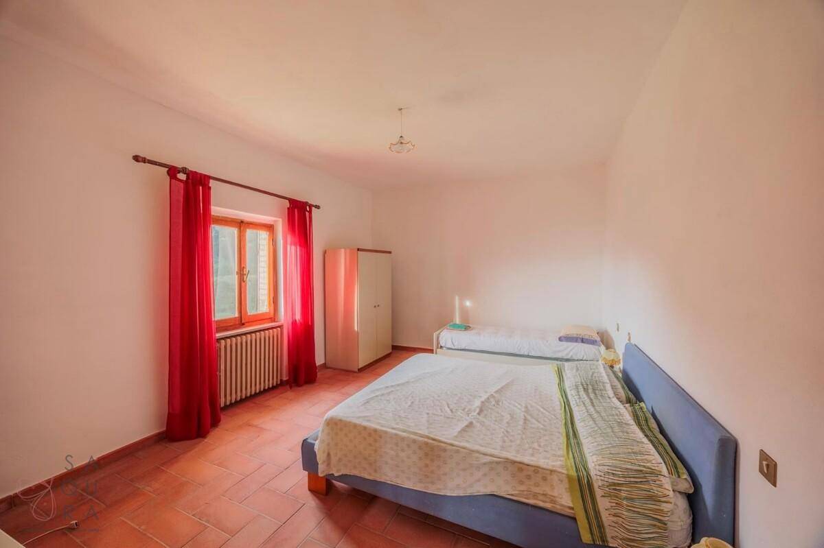 Geräumiges Schlafzimmer mit zwei Betten, Terrakottaboden und roten Vorhängen am Fenster.