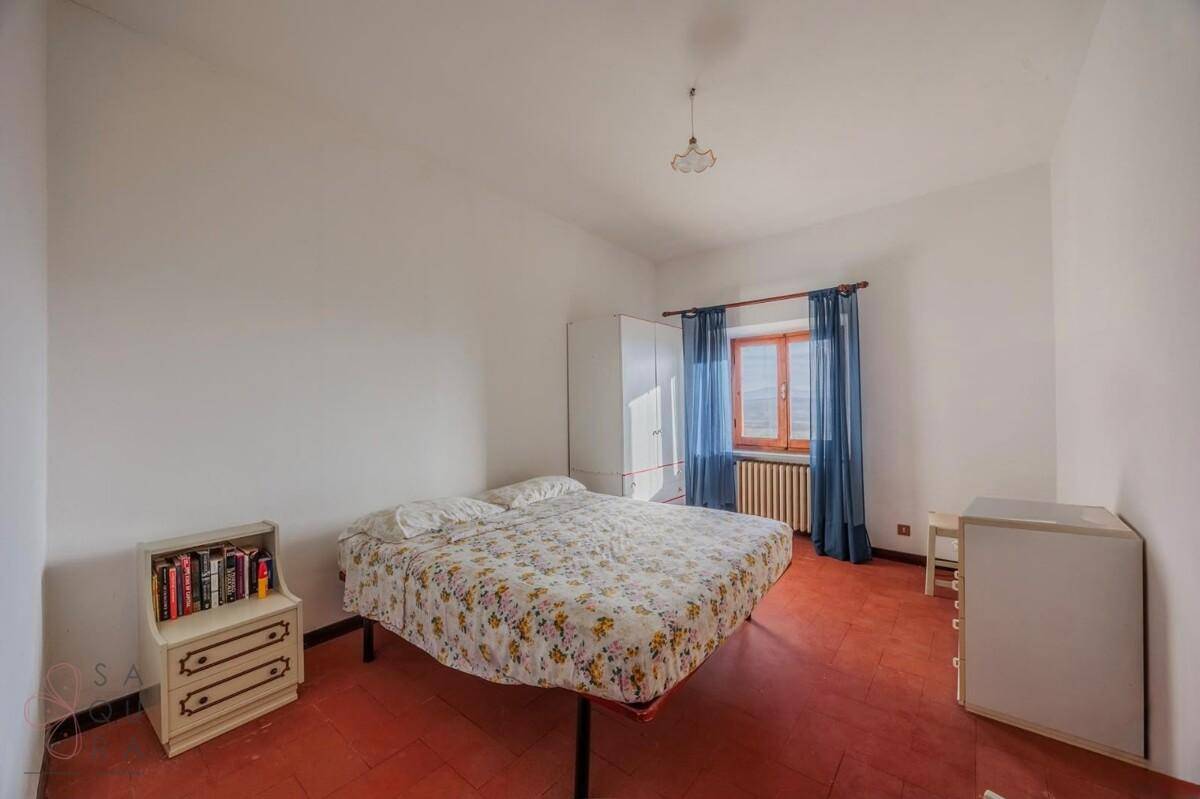 Einfaches Schlafzimmer mit Doppelbett, Terrakottaboden und blauen Vorhängen am Fenster.