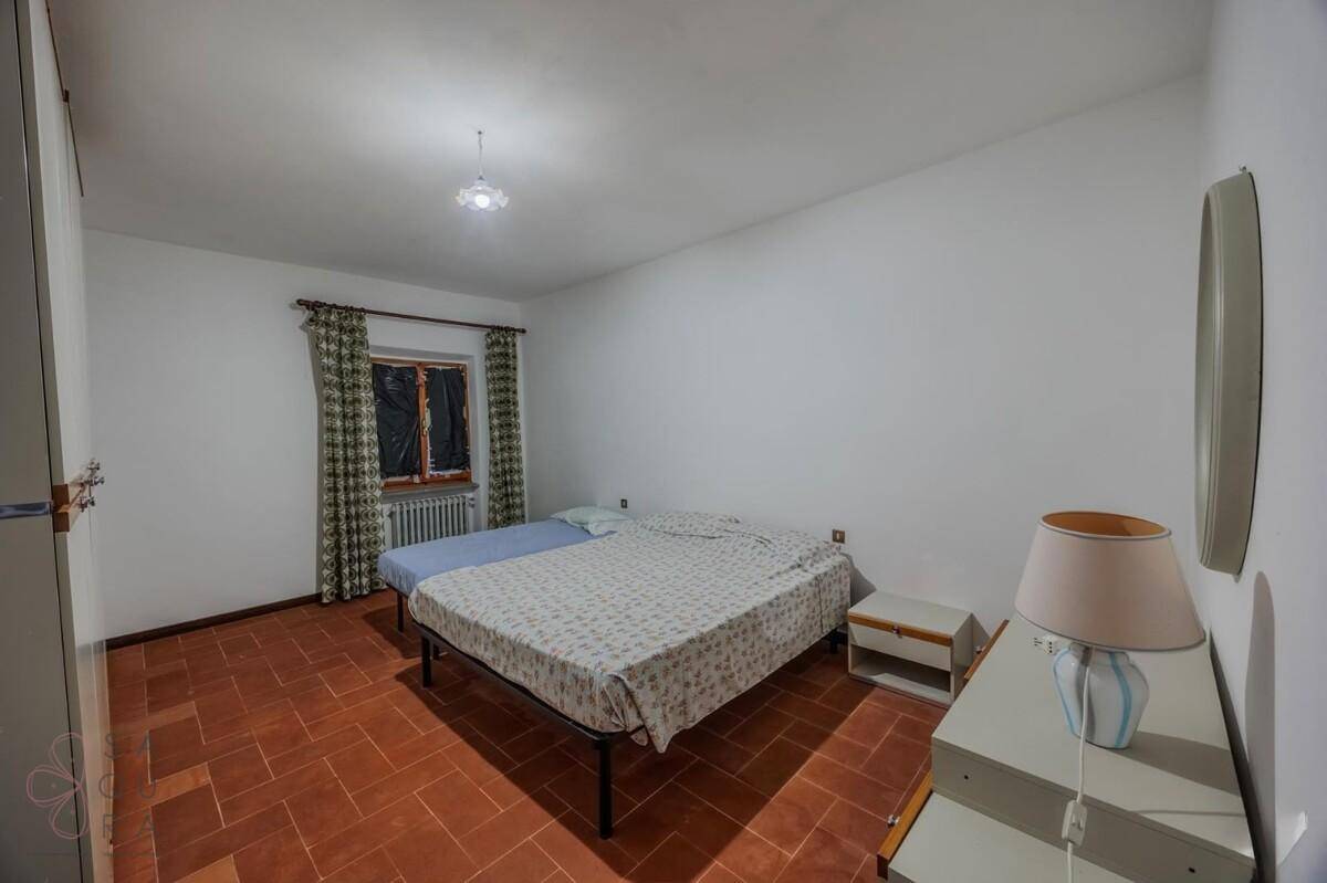 Schlafzimmer mit zwei Betten, Terrakottaboden und schlichten Möbeln, gut erhalten.