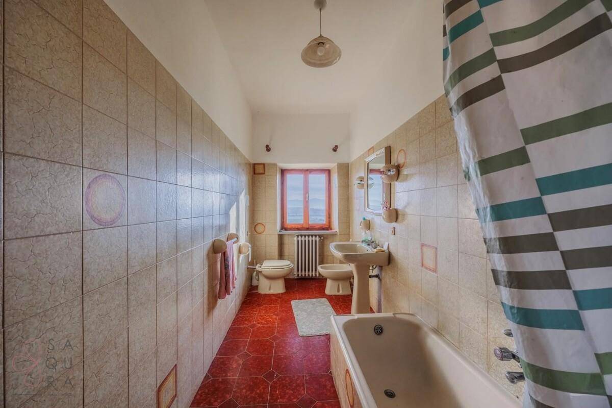 Langes Badezimmer mit beigen Fliesen, Badewanne, Bidet und Fenster, im Stil der 80er Jahre.