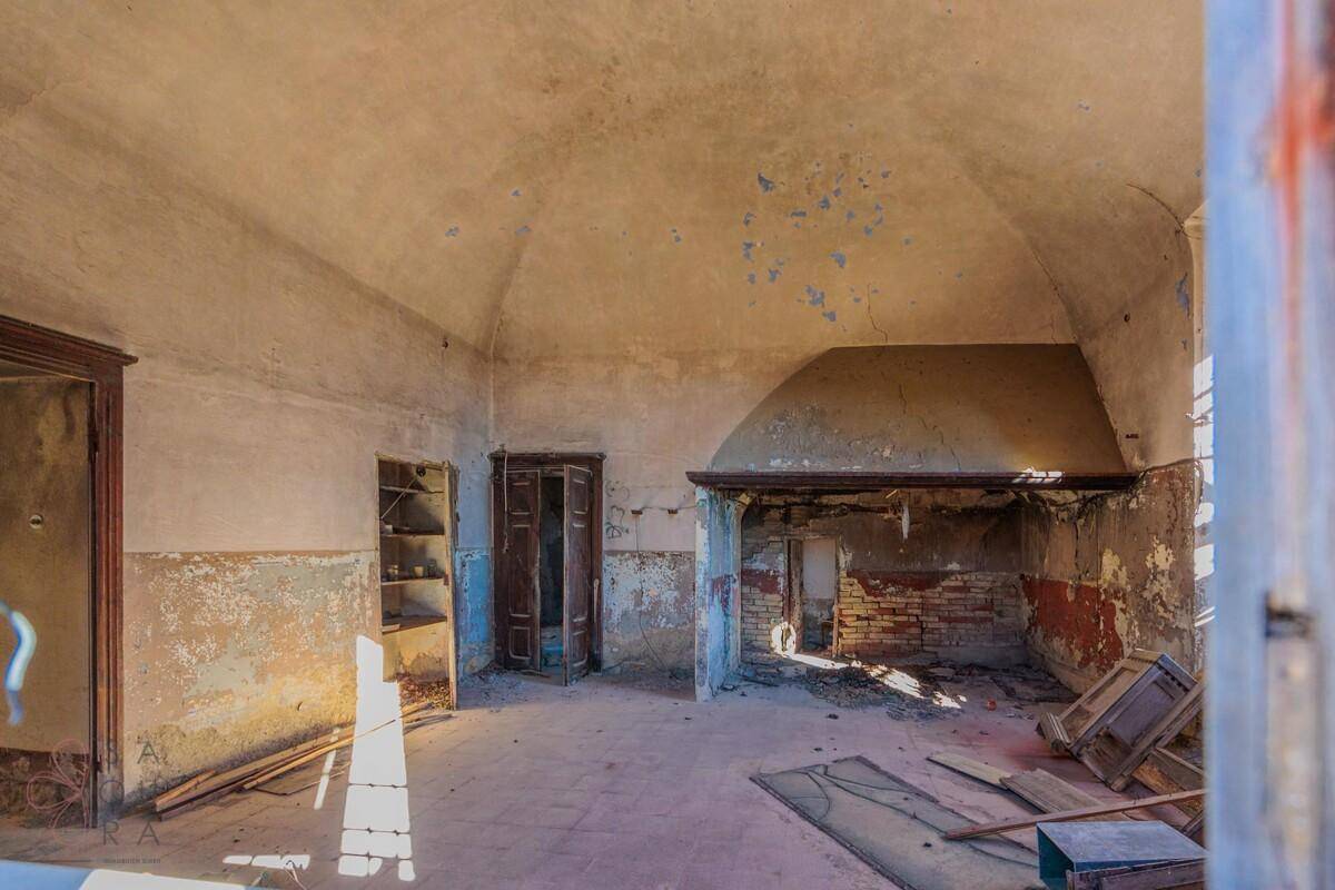Verfallener Innenraum mit gewölbter Decke, großem Kamin und abblätternder Farbe.